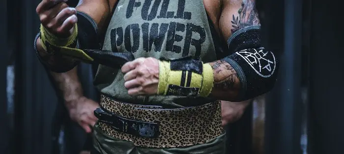 Man wearing powerlifting belt, putting on wrist straps.