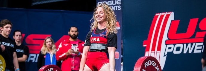 Blonde woman at a powerlifting competition, finishing a deadlift.