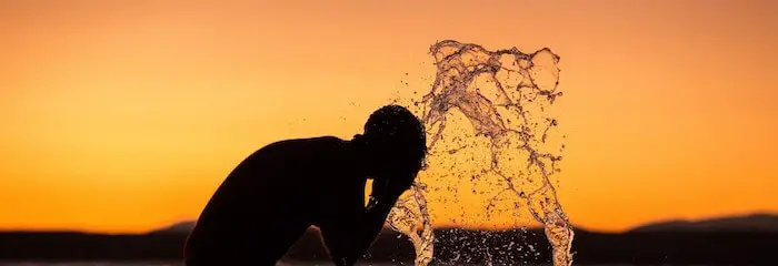 A man washing his face in a lake or river.